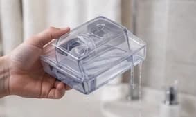 A CPAP humidifier chamber being rinsed at a sink with water draining